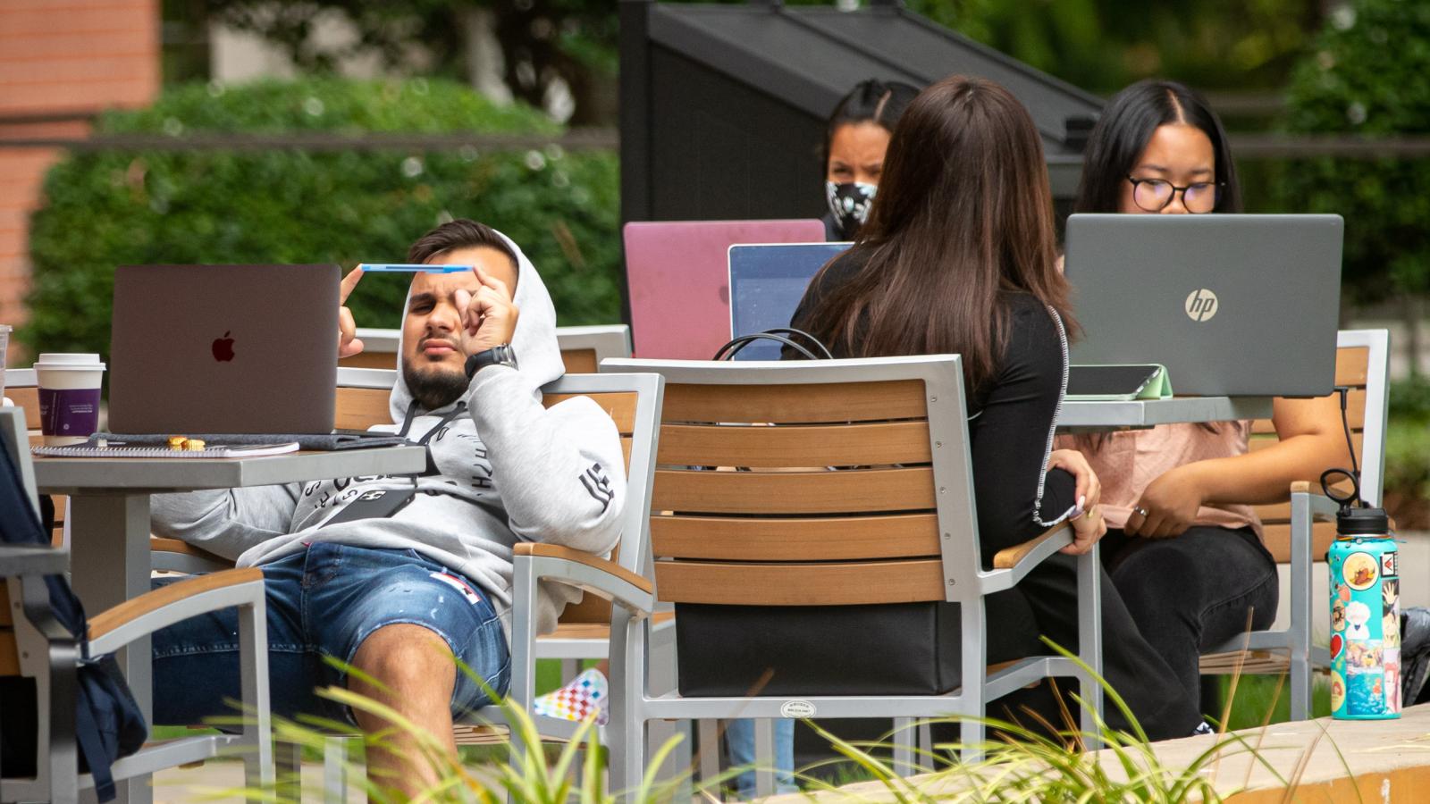 Students sitting with laptops in chairs outside wit
