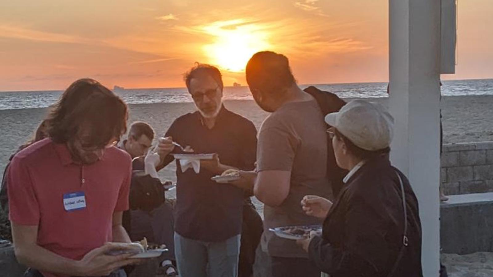 people eating dinner on the beach at sunset
