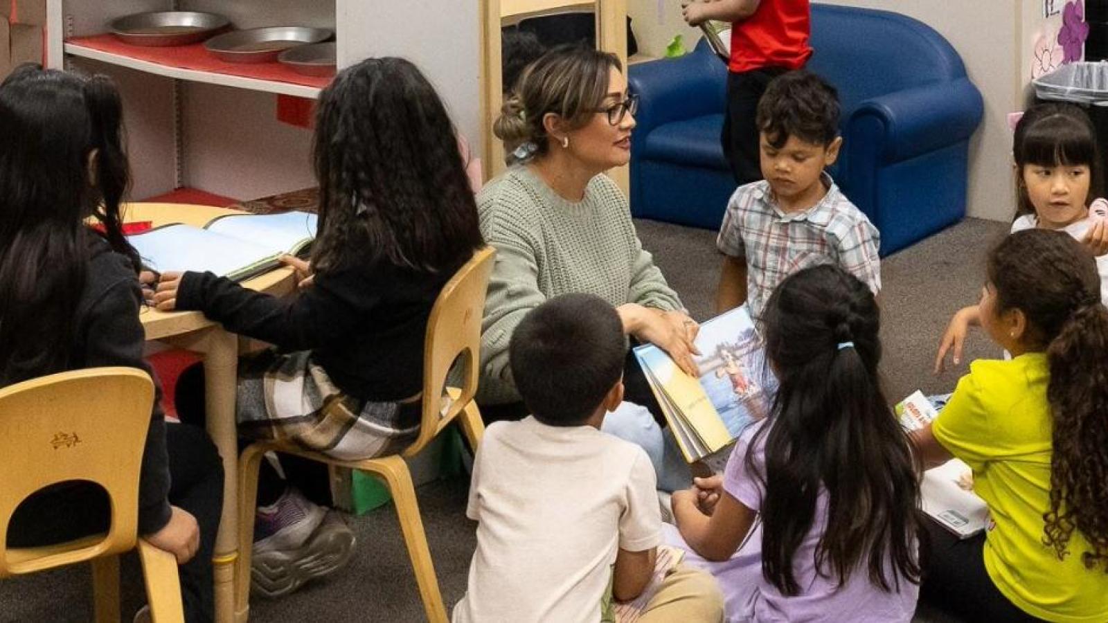A teacher sits with students in a classroom for a lesson.
