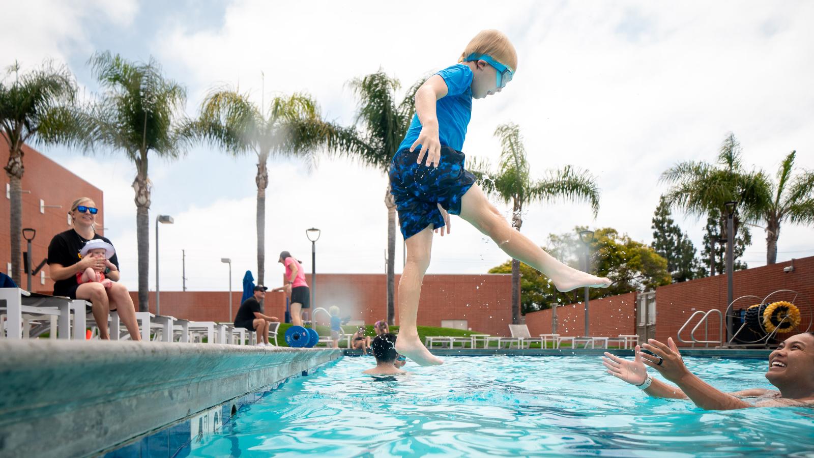 A child jumps into a pool as a counselor stands with outstretched hands