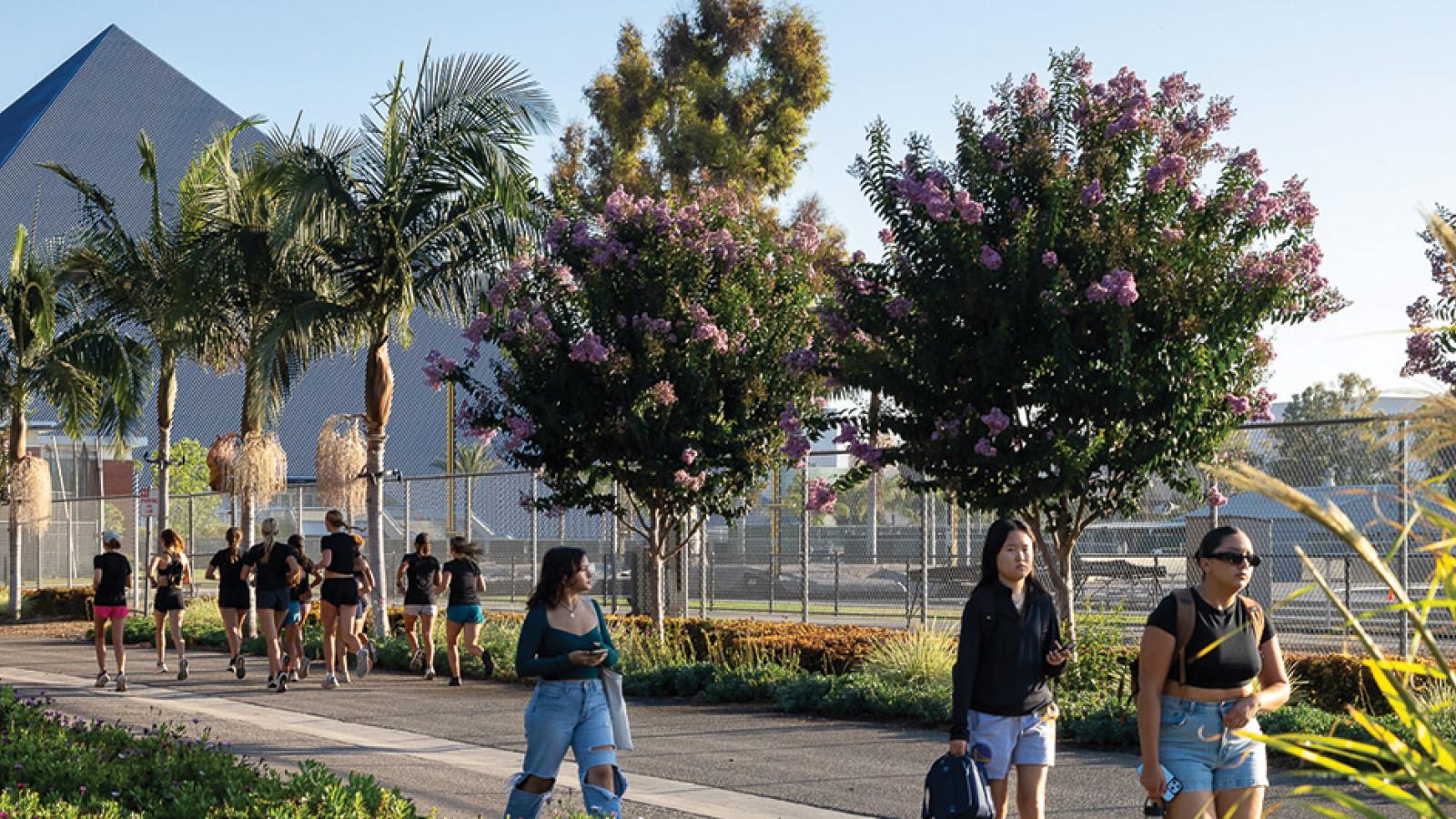Runners and students walk on path in front of pyramid