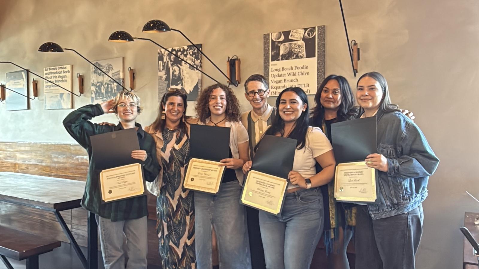 group of people standing in front of wall holding award certificates.