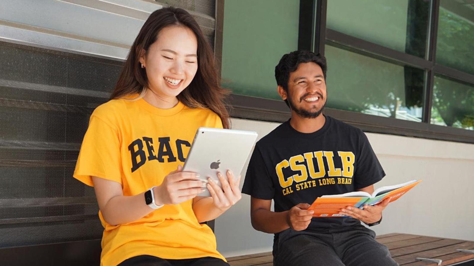 smiling students reading a tablet and a textbook