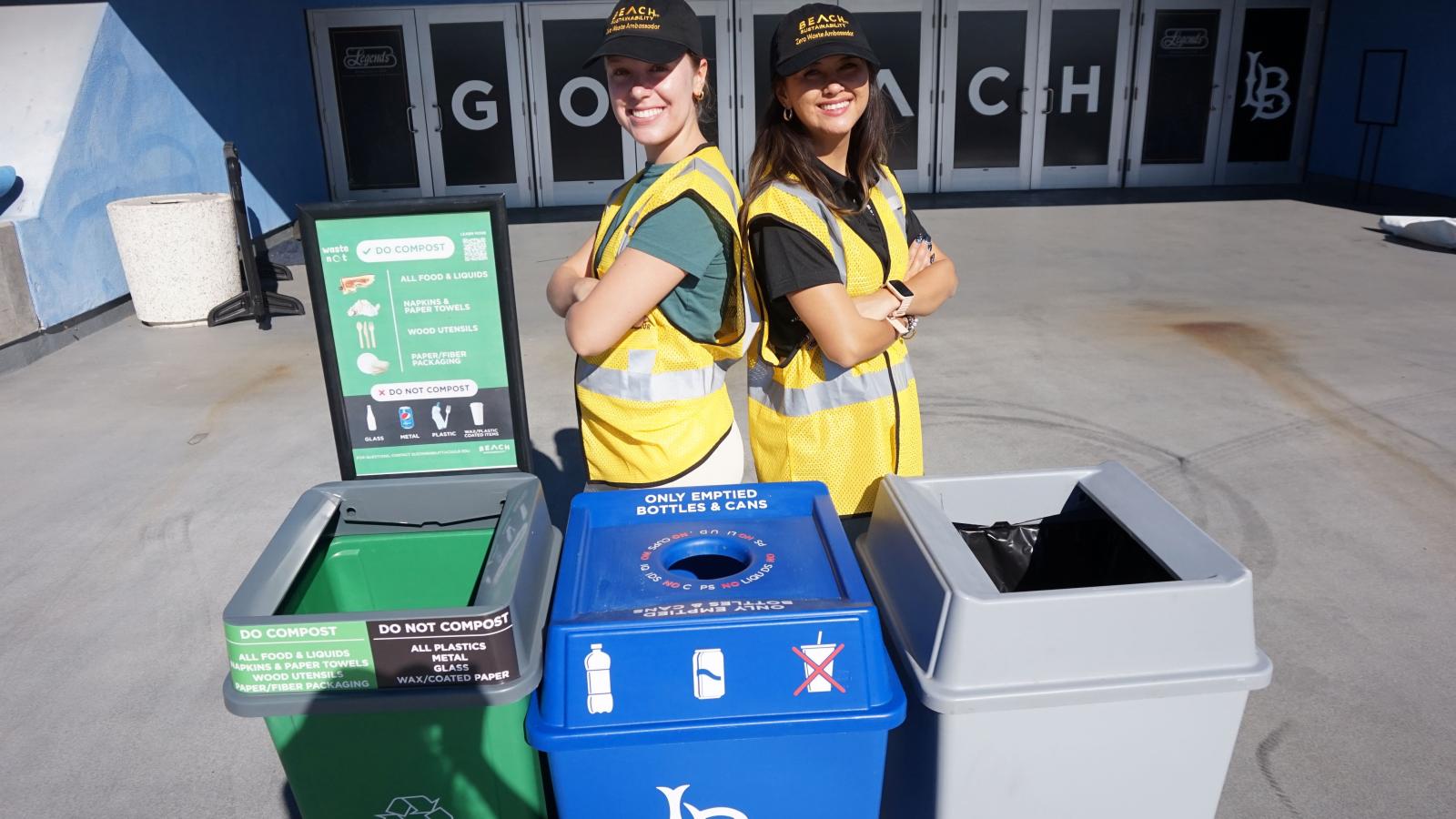 Two students standing back to back with a blue, green, and gray bin.