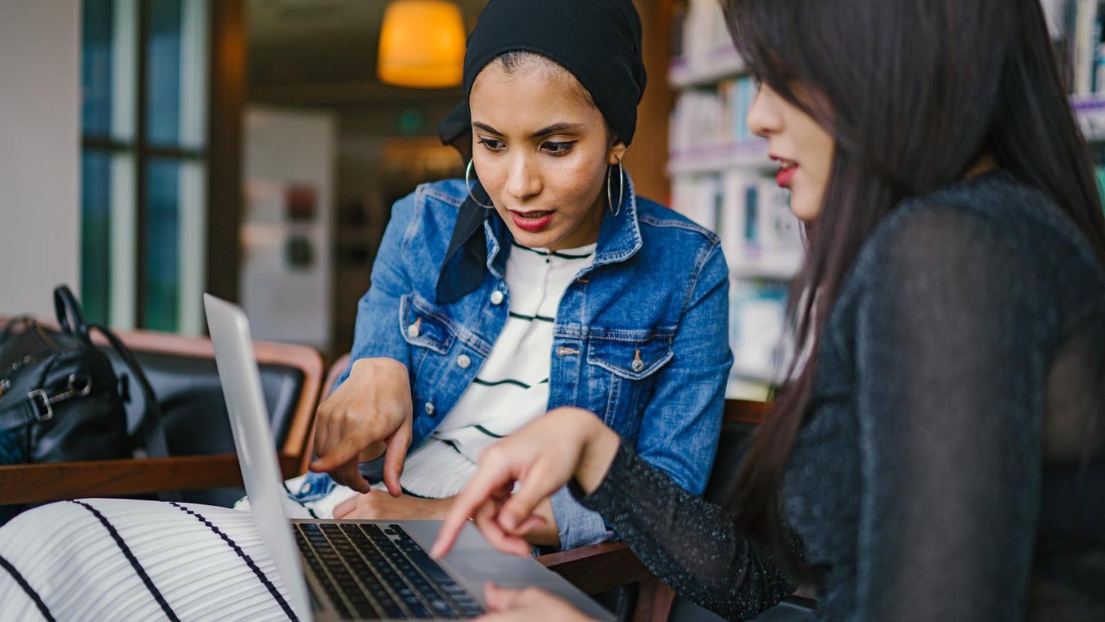 latinx woman and asian woman pointing and looking at laptop