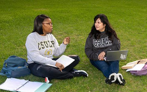 Students sit on grass while working on computers