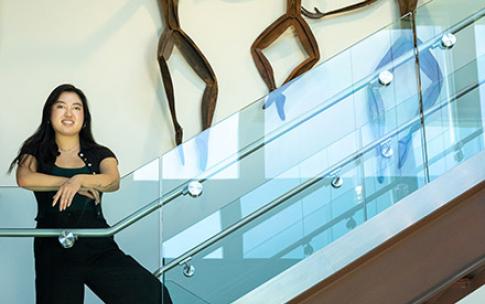 Student stands on staircase with blue glass railing