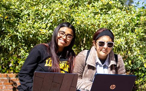 A student mentor with mentee, on a bench with laptops.