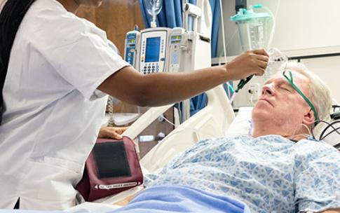 A student nurse at CSULB checks on a mock patient in a hospital bed at the school.