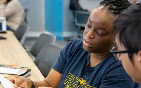 A woman in a "Rams Track & Field" shirt reviews a tax document with an accounting student at the VITA lab.