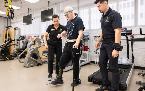 Two students helps a Neuro Lab client as he uses a cane to walk