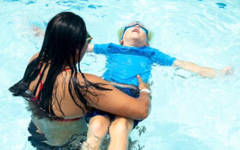 An adult holds child floating on back in water
