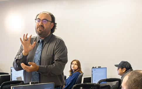A person wearing glasses and a tie speaks in front a class