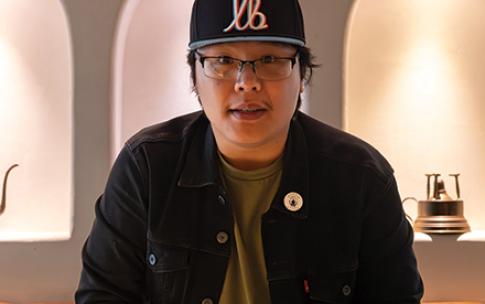 Person stands at a restaurant table holding a phone while preparing to eat from a bowl.