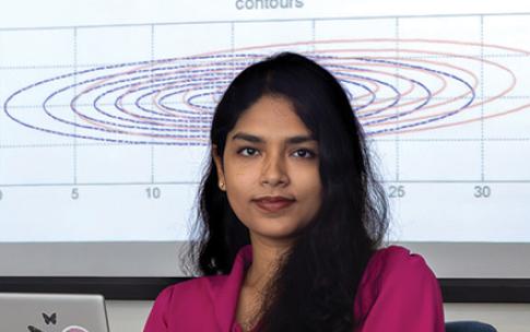 A student with long hair at a computer with a slide projected behind her
