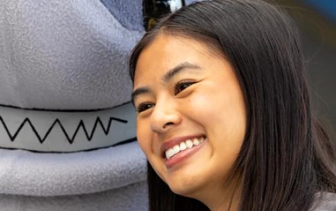 A person with long hair poses with a mascot