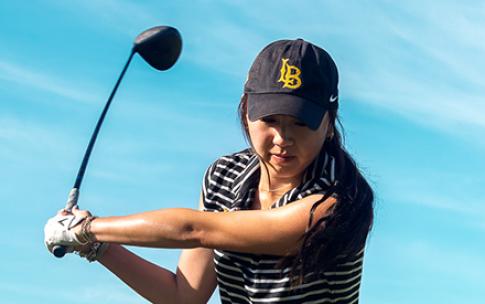A person follows through on a golf swing under a blue sky.