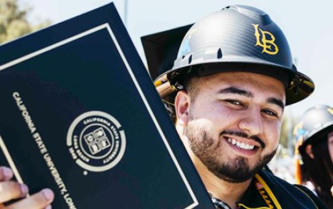 CSULB graduate with hard hat holding his diploma