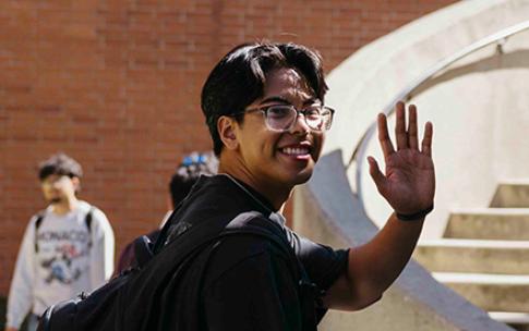Student waving in front of stairs