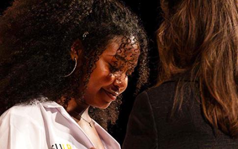 A student receiving a faculty member's help donning a lab coat