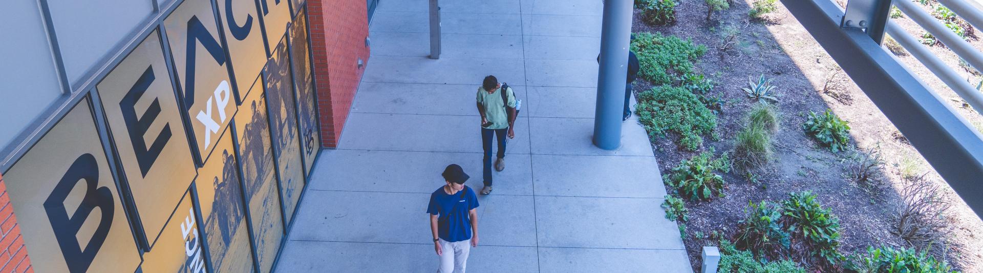 Students walk back the College of Professional and Continuing Education. On the window of the building, a decal displays the Beach XP logo.