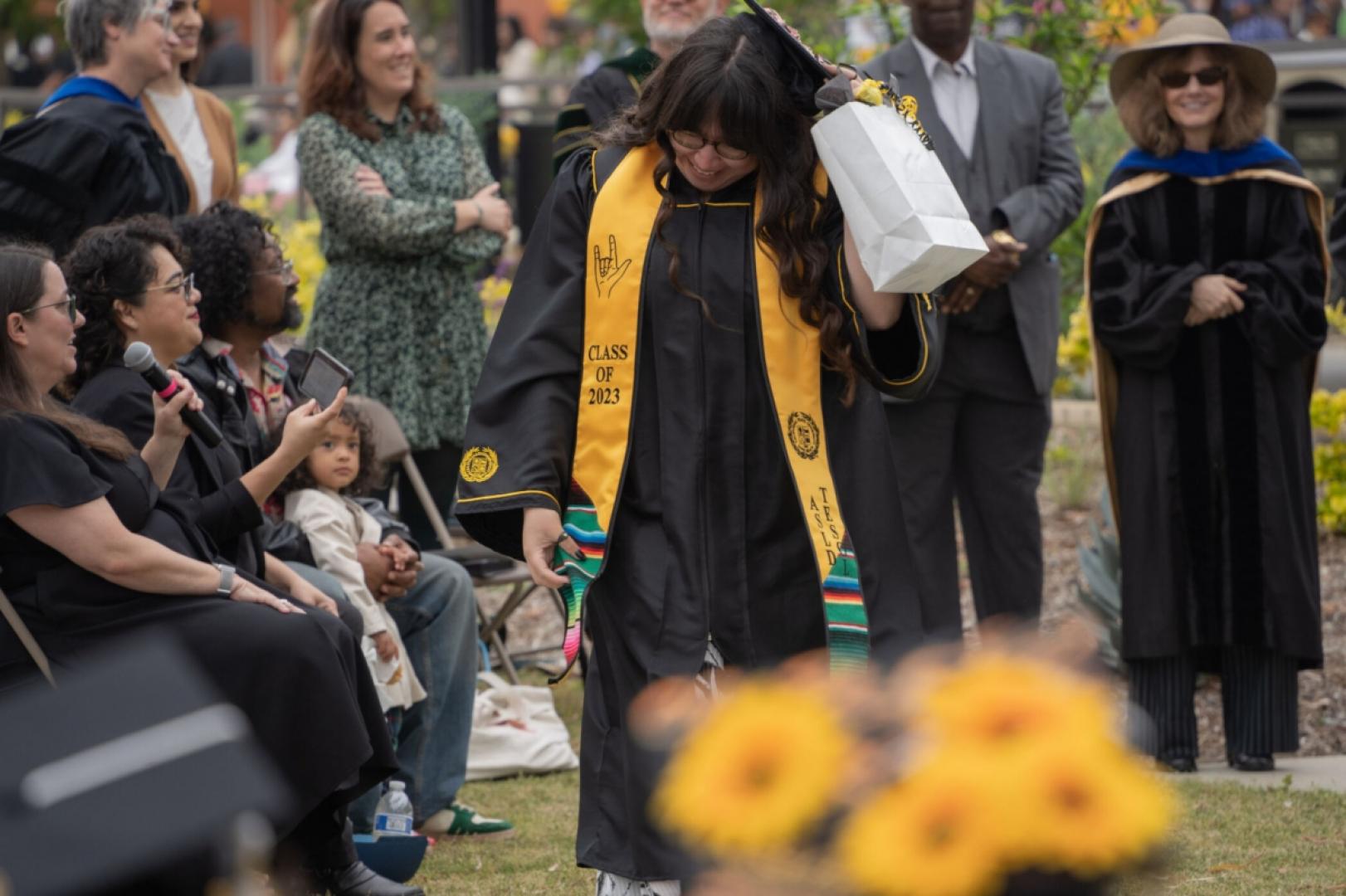 Student walks forward through graduation ceremony wearing grad gown and stoll.