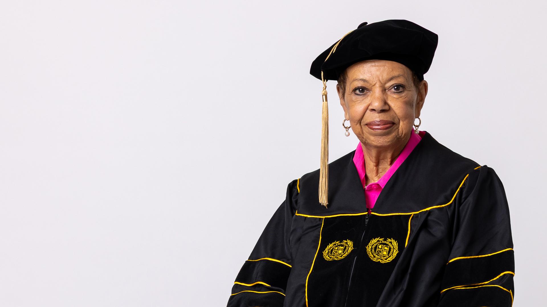 An older person wearing academic regalia with embroidered seals sits facing forward