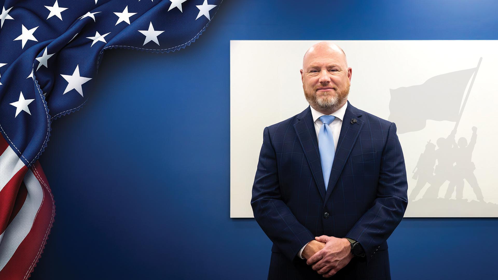 Marshall Thomas stands in front of silhouette of Marines with flag