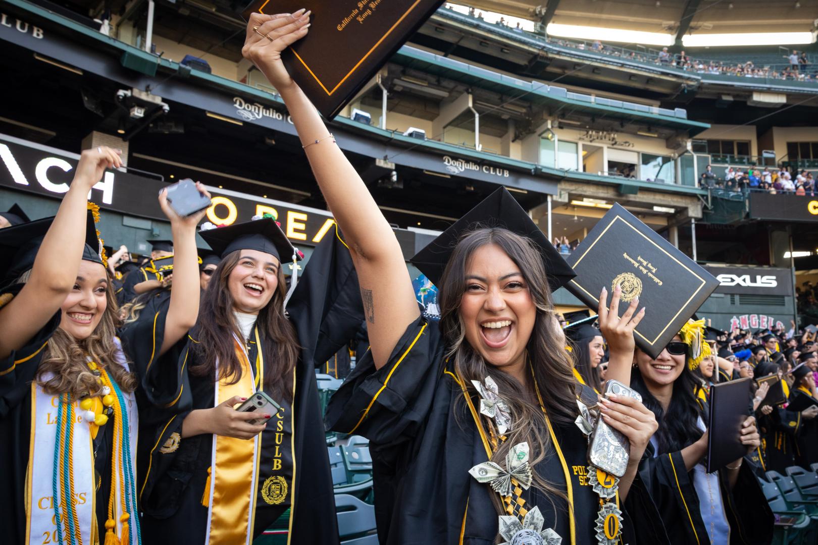 CSULB graduates celebrating and holding diplomas at commencement