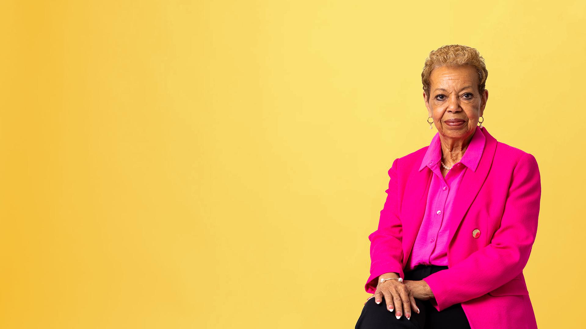 A person wearing pink looks into camera against yellow background