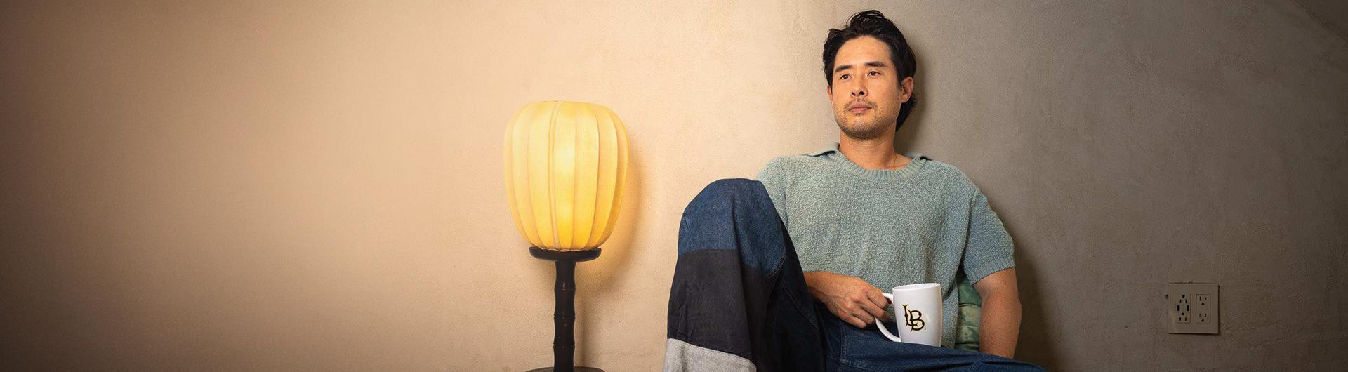 Actor Raymond Lee '08 sits on the floor, next to a lamp