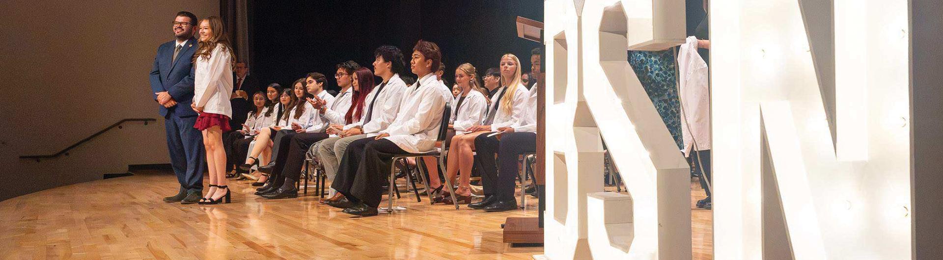 Students on stage wearing white lab coats