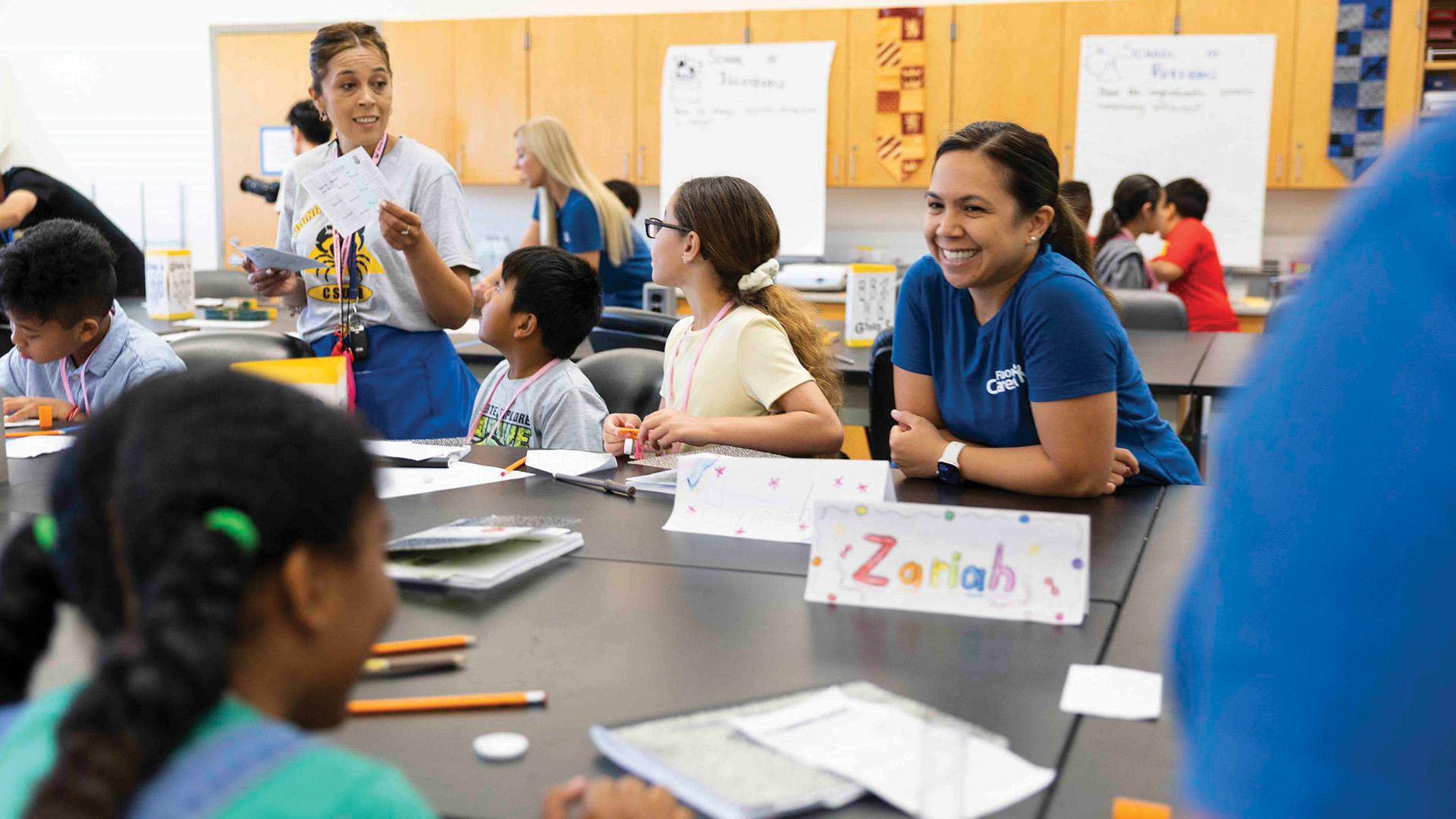 Two people smile and chat with children at a table