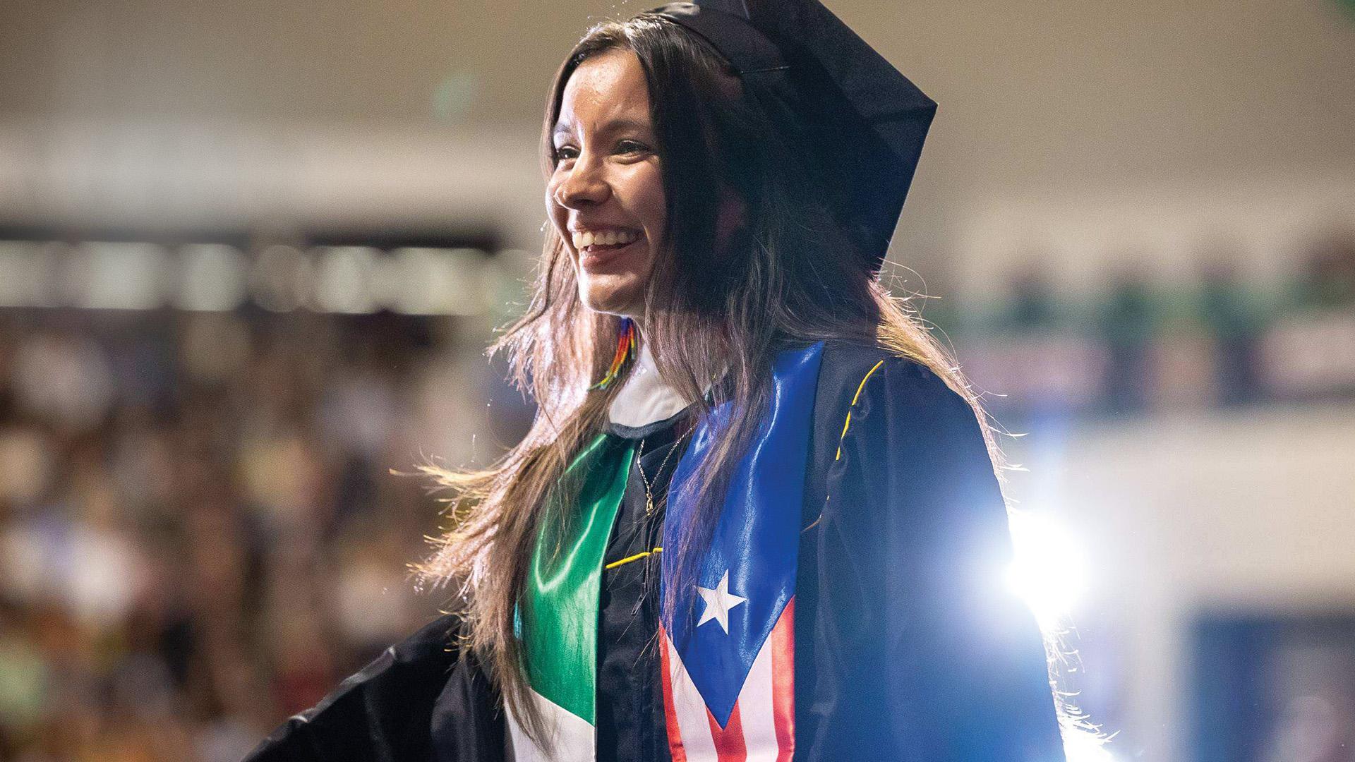 A graduate wearing regalia and a sash inspired by the flags of Mexico and Puerto Rico