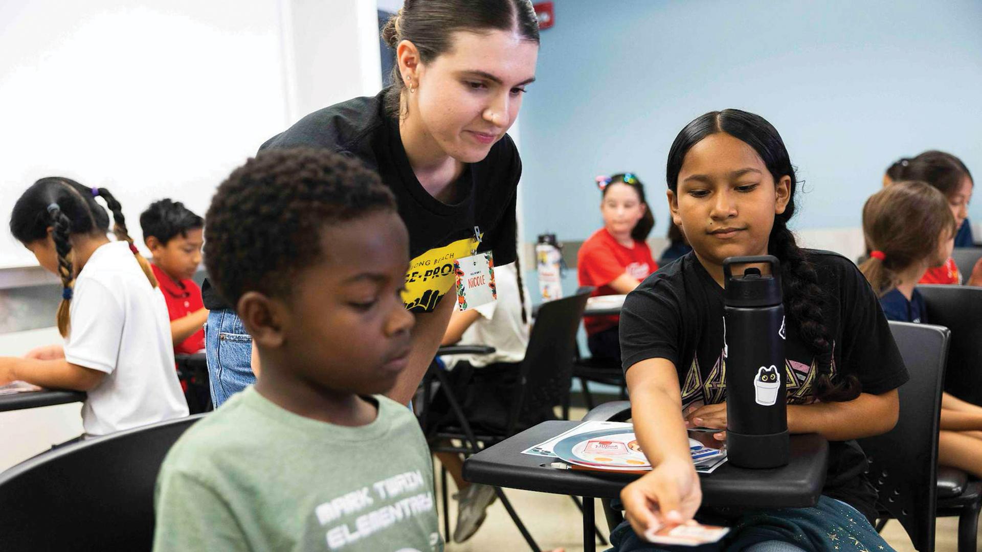 A person stand between two children in a classroom setting
