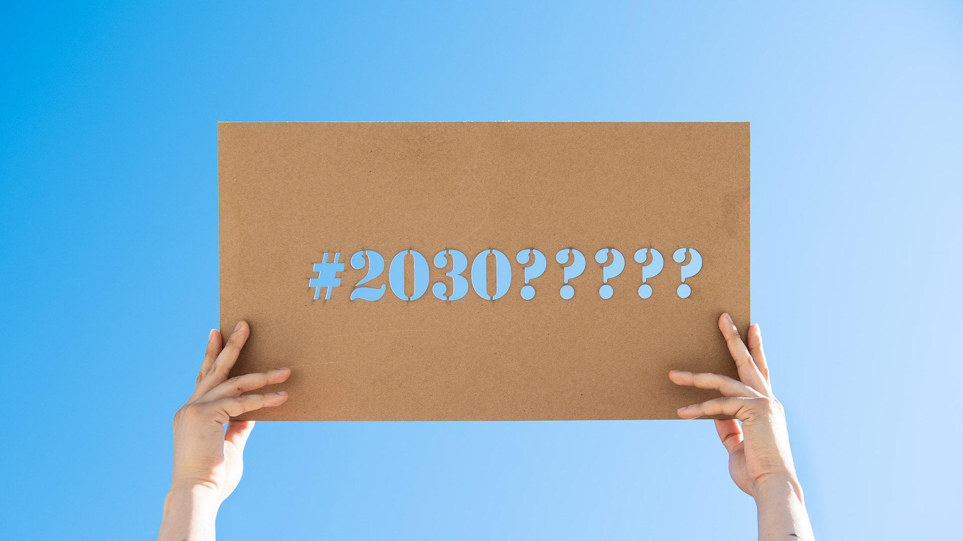 Hands holding a cardboard sign that says: #2030????? 