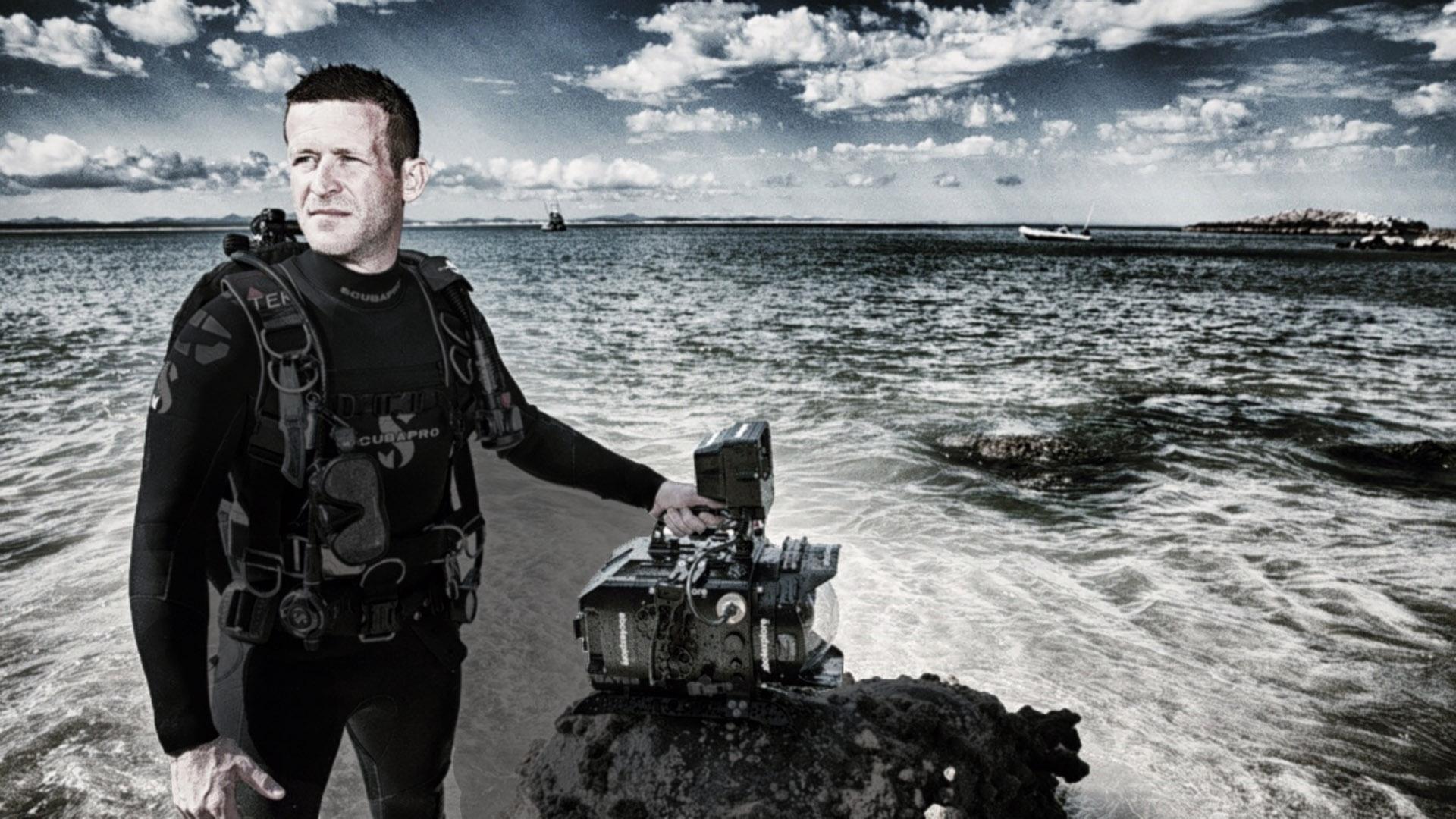 Alumni that is an underwater cinematographer poses with his camera.