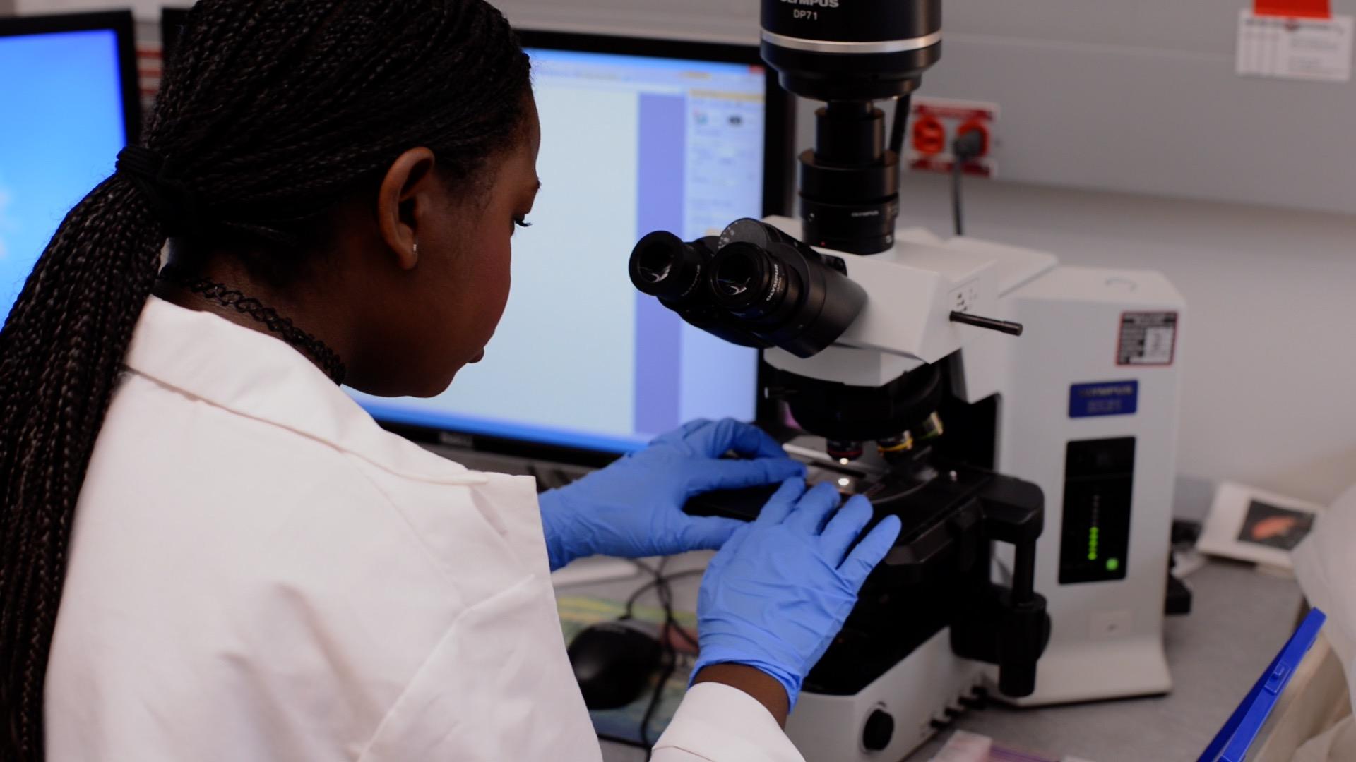 BUILD Scholar Rhea Comfort-Addo inserts slide into a microscope.