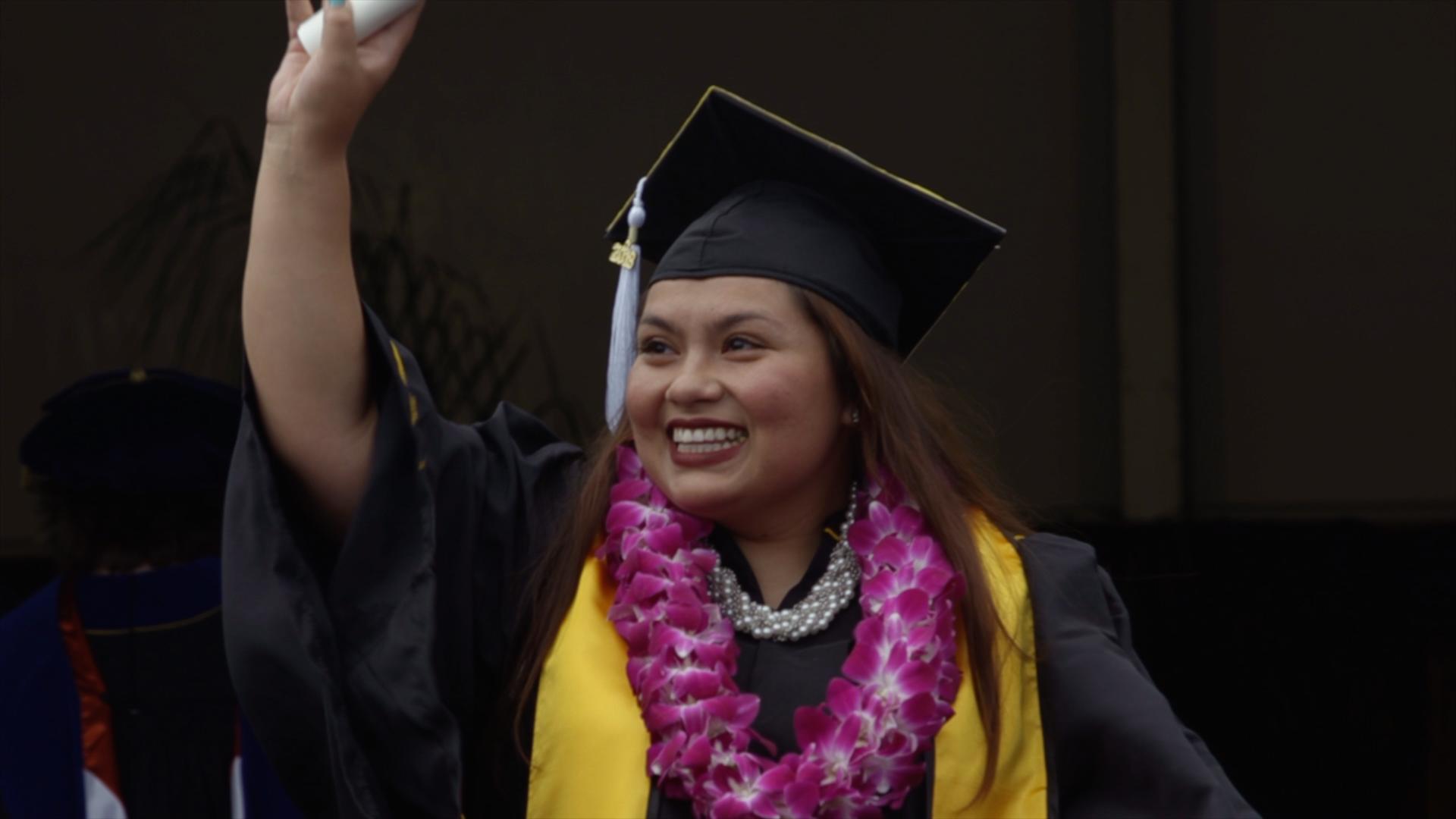 A new graduate holds her degree up in the air.