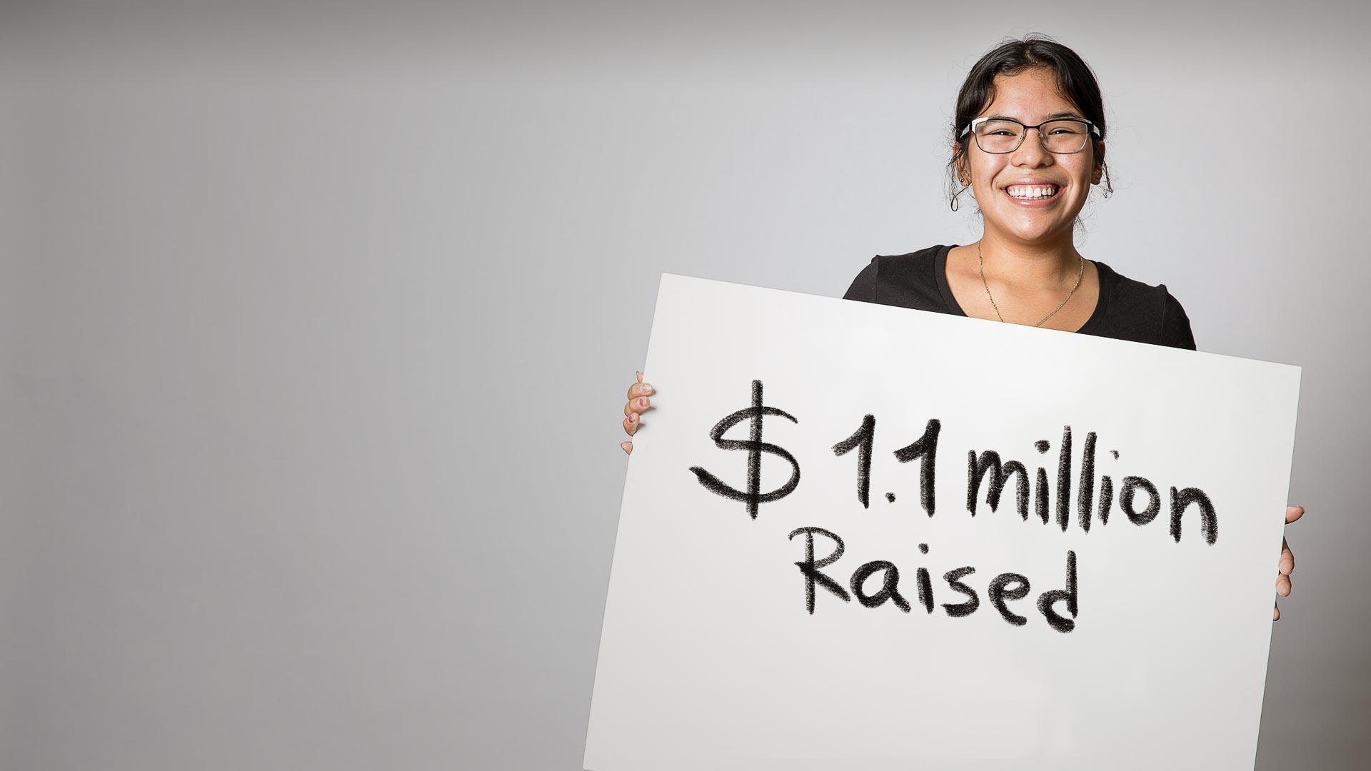 Student holds a sign: 1.1 million raised