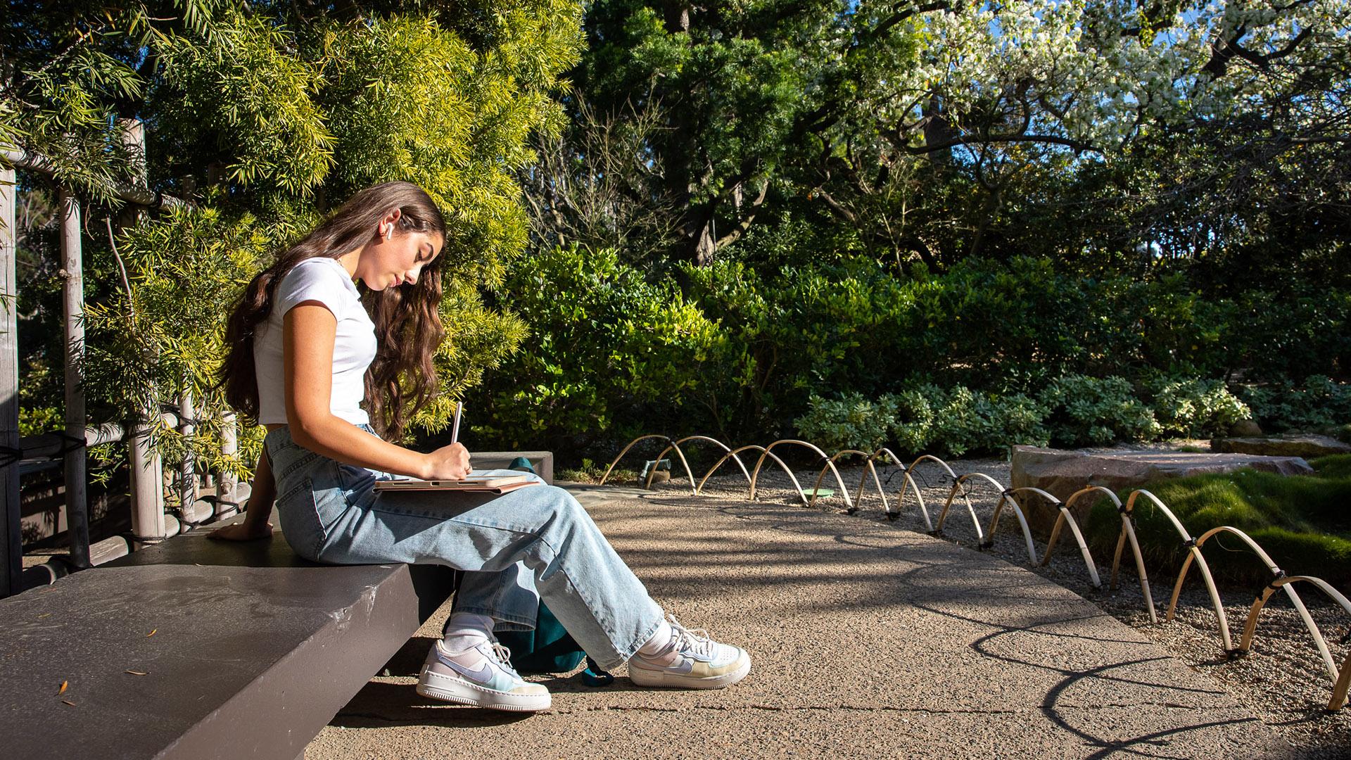 Female student sits on a bench at the Japanese Garden