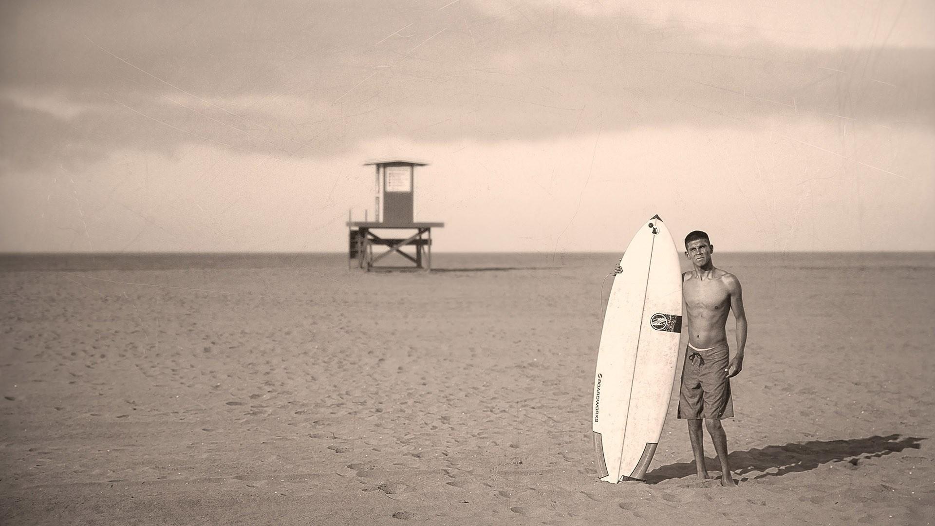 Jake Pacheco stands on beach with his surfboard