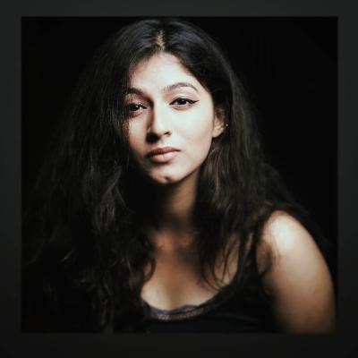 Bhargavi Sardesai Headshot. Her hair is down, she is in a black tank top against a black background.