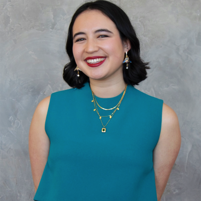 Female presenting person smiling with short black hair and light skin, wearing turquoise.