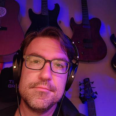 Nick looks at the camera there are 3 guitars behind him