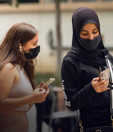 Two students with masks on, check their phones