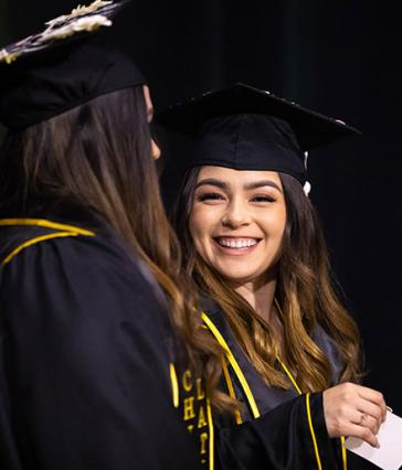 Hispanic female grad smiles at another student