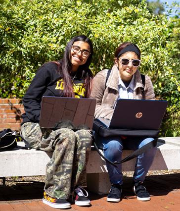 A student mentor with mentee, on a bench with laptops.