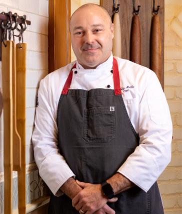 Disneyland chef Toby Hollis stands against a brick wall with wooden utensils hanging beside him.