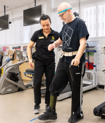 Romina Silva helps a Neuro Lab client as he uses a cane to walk